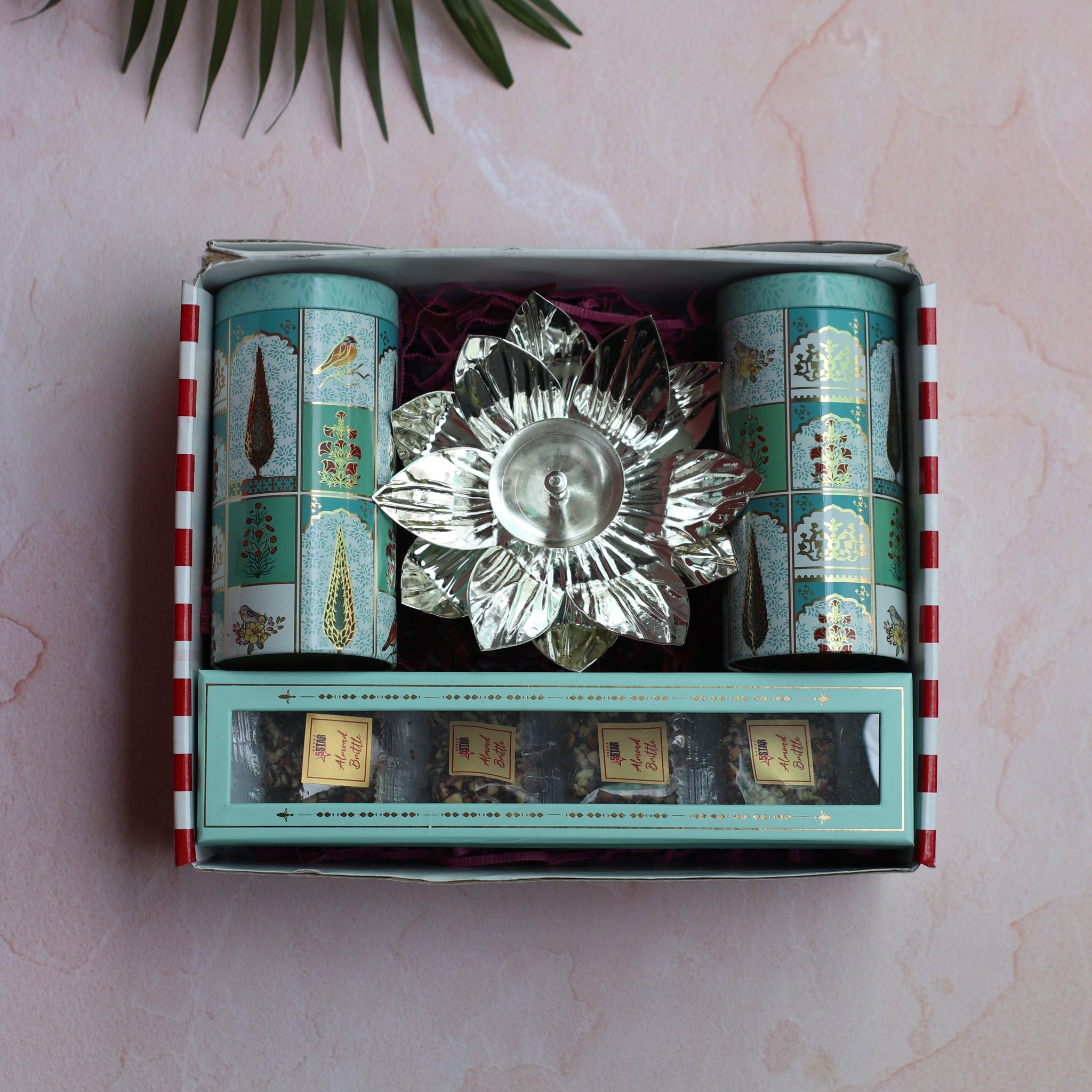 Decorative box with a crystal dish and green packaging on a light pink surface with a leaf.