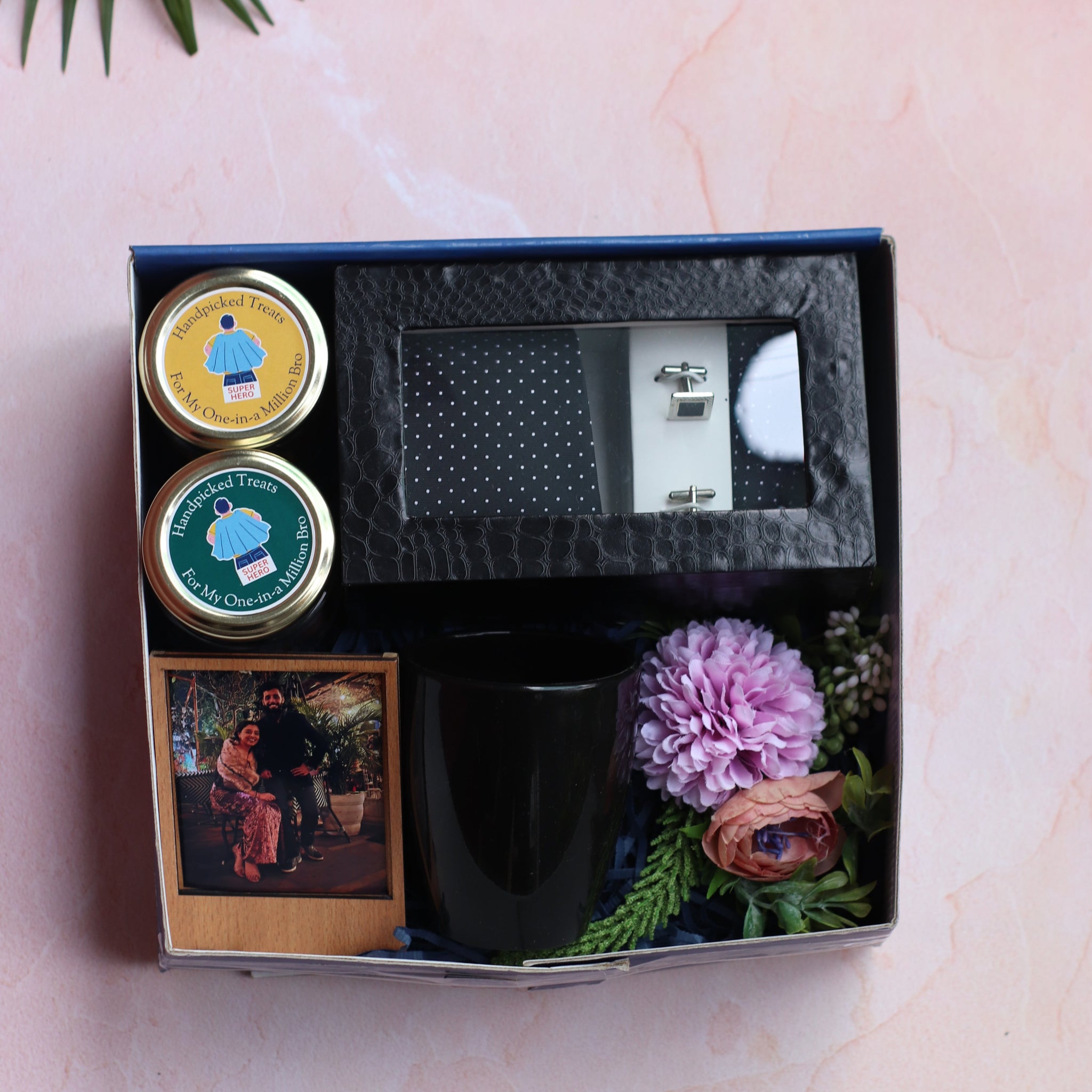 Gift set with a mug, small plant, and decorative items in a box on a light pink background.