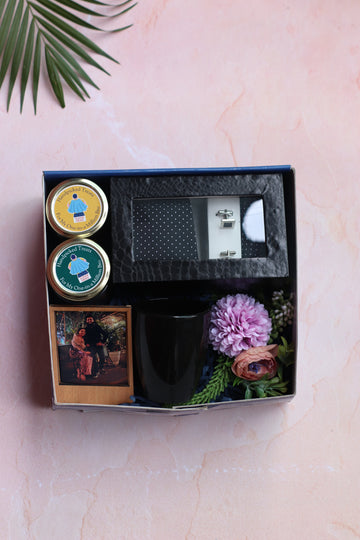 Gift set with a mug, small plant, and decorative items in a box on a light pink background.